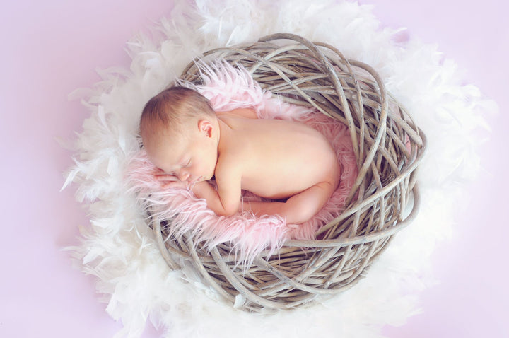 baby sleeping in a basket and a round feather surrounding the basket|photo of a man raising baby under blue sky|man kissing woman