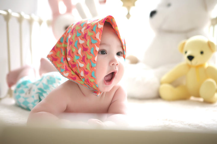 toddler wearing head scarf in bed|baby sitting on green grass beside bear plush toy at daytime