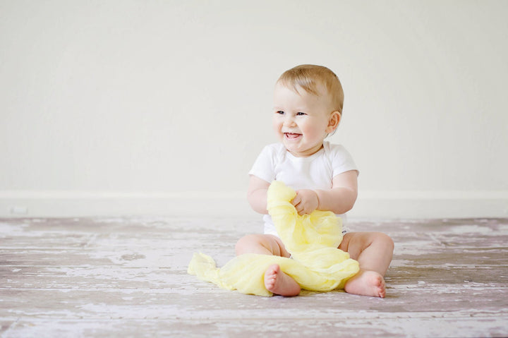 toddler sitting while smiling|toddler in yellow top and hat holding fruit