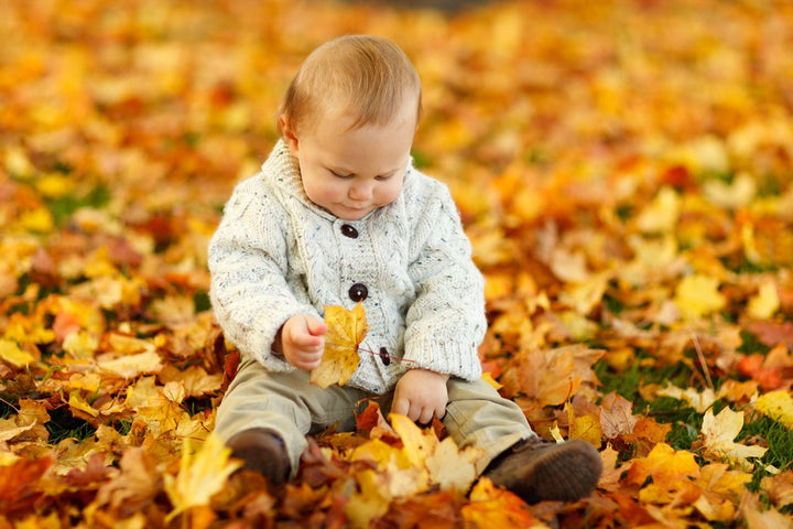 Bambino con morbida maglieria tra le foglie d'autunno – consigli per vestire il bambino in autunno