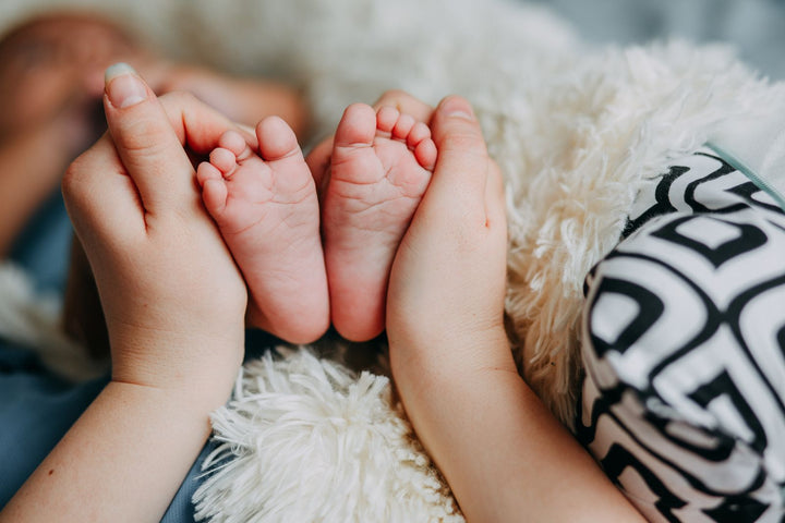 Main de parent tenant les petits pieds d'un nouveau-né dans la douceur – prénoms préférés des familles Babanono en août 2026