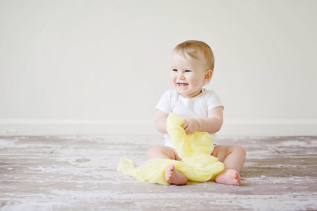 toddler sitting while smiling|toddler in yellow top and hat holding fruit