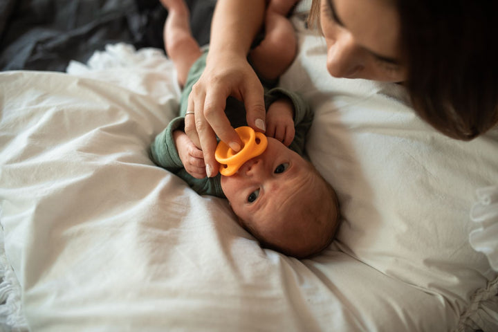 Bébé allongé sur un lit tenant sa tétine dans une lumière douce – à quel âge donner une tétine à bébé