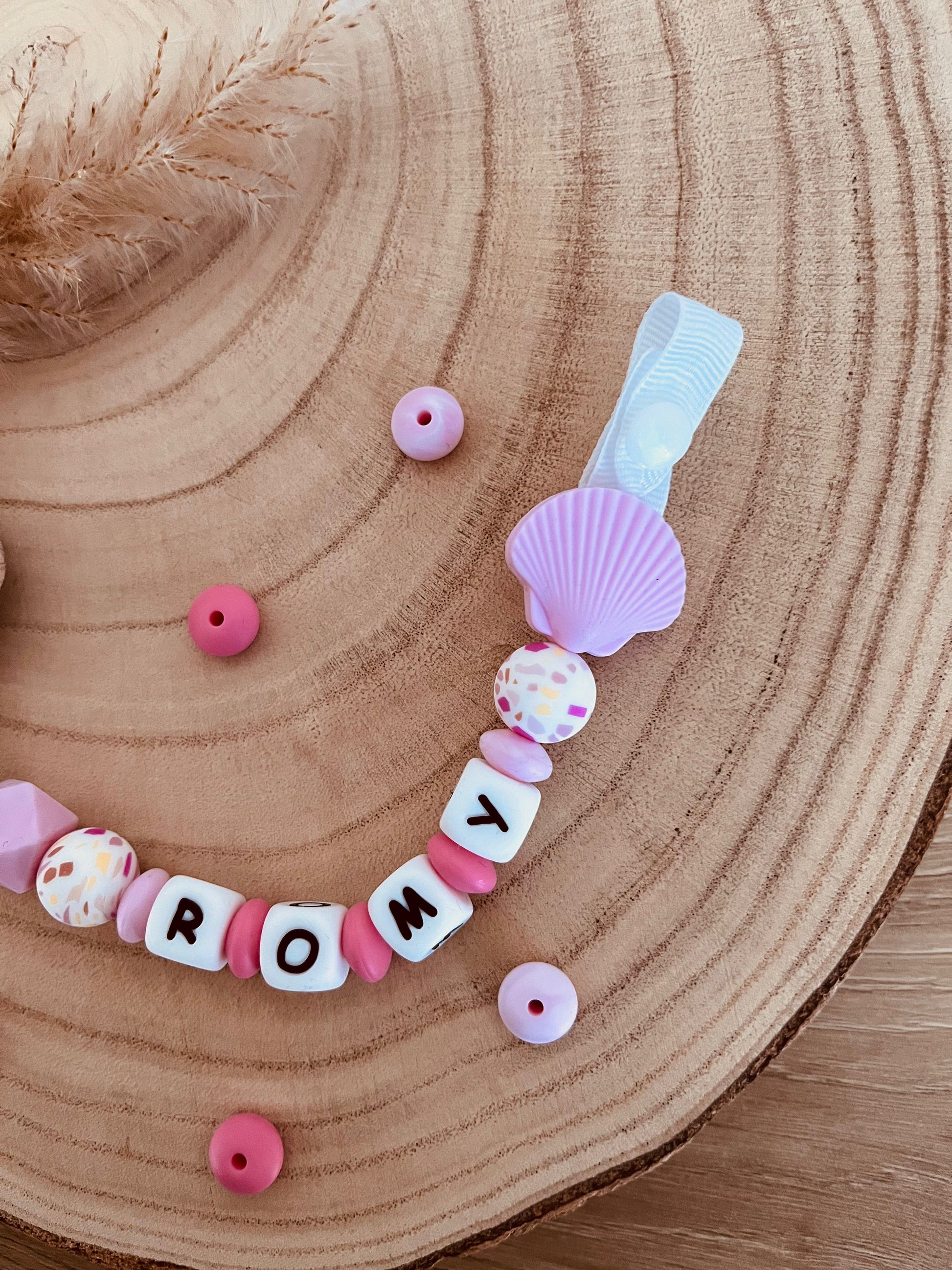 Détail du pendentif coquillage et du clip en bois de hêtre de l'attache tétine personnalisée rose