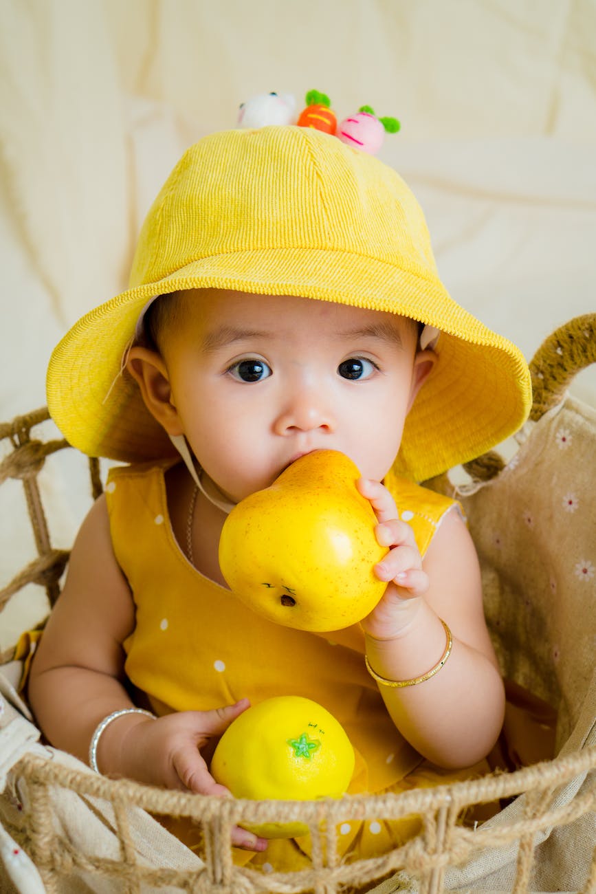 toddler in yellow top and hat holding fruit