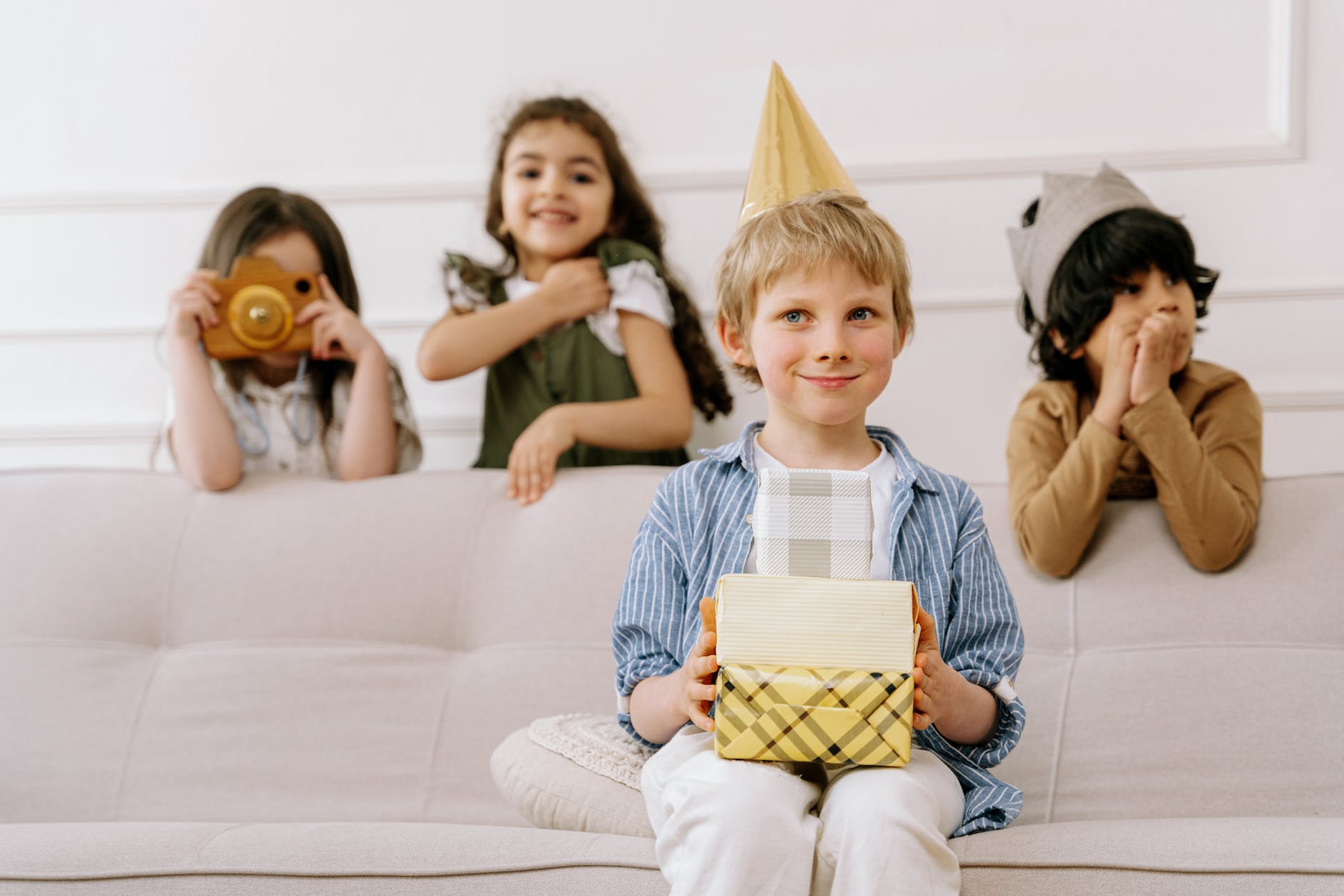 children behind a boy sitting on a couch holding gift boxes